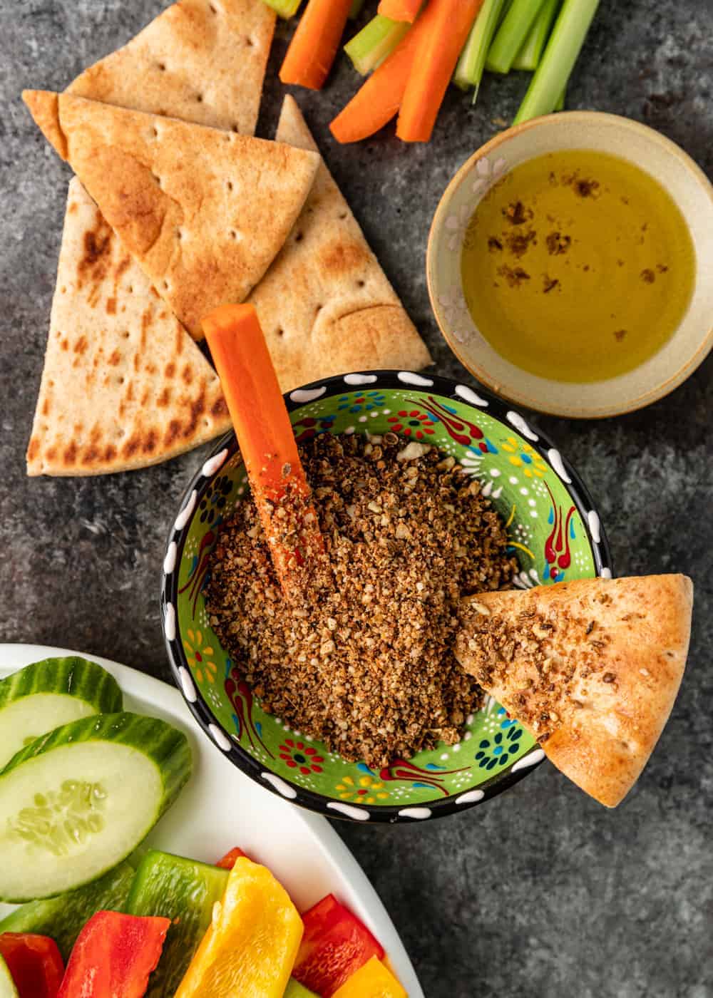 overhead image: Egyptian dukkah in green pottery bowl with carrot stick and slice of pita bread
