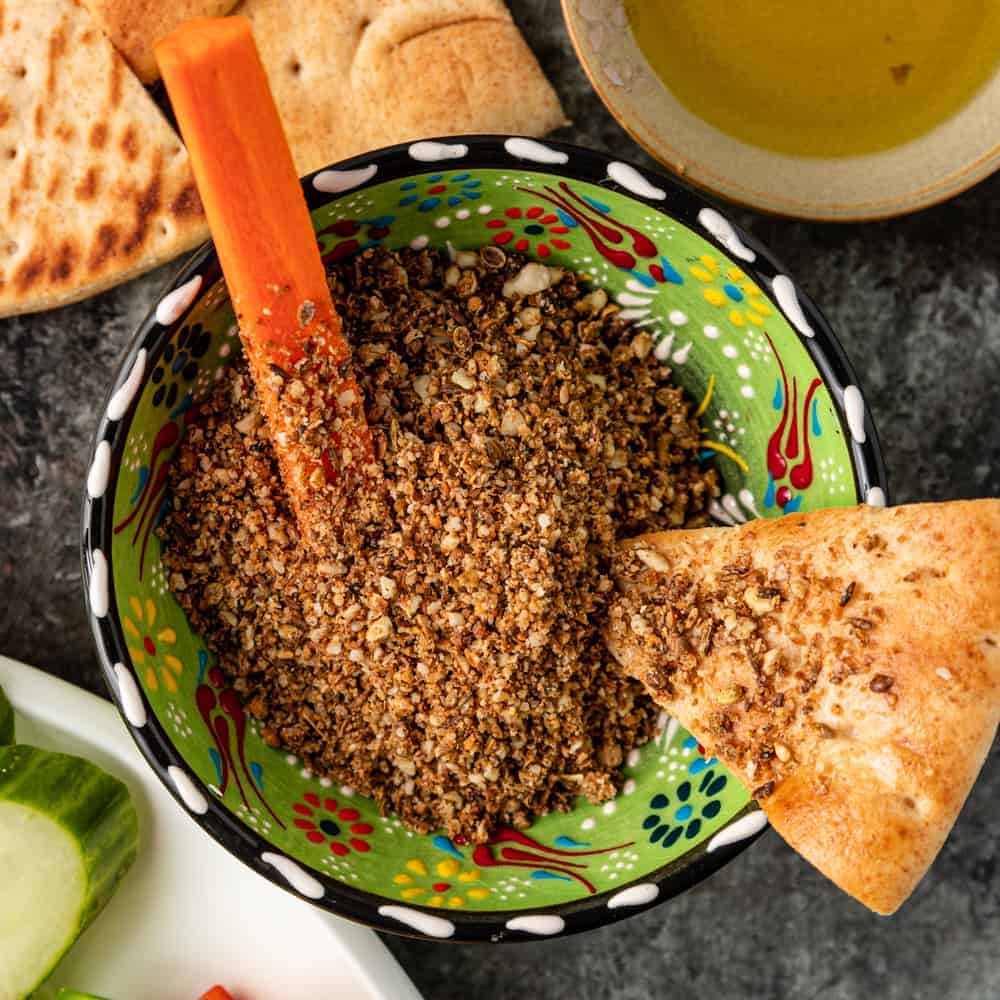 overhead image: Egyptian dukkah in a green pottery bowl with slice of pita bread