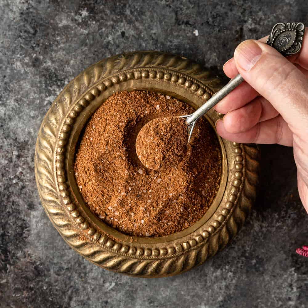 overhead image: man's hand holding spoonful of Lebanese 7 spice above a small dish of the seasoning blend