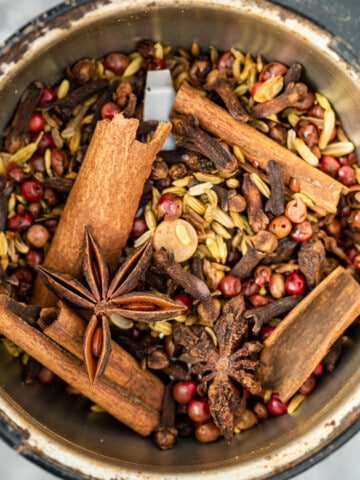 close up of cinnamon sticks, star anise, fennel seeds, cloves, and peppercorns in a spice grinder
