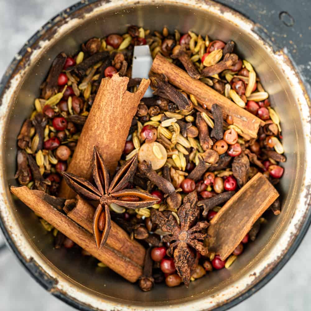close up of cinnamon sticks, star anise, fennel seeds, cloves, and peppercorns in a spice grinder for chinese five spice recipe
