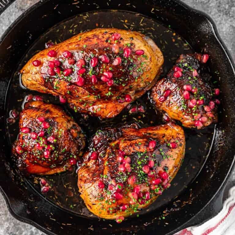 overhead image: 4 pieces of pomegranate chicken in cast iron skillet