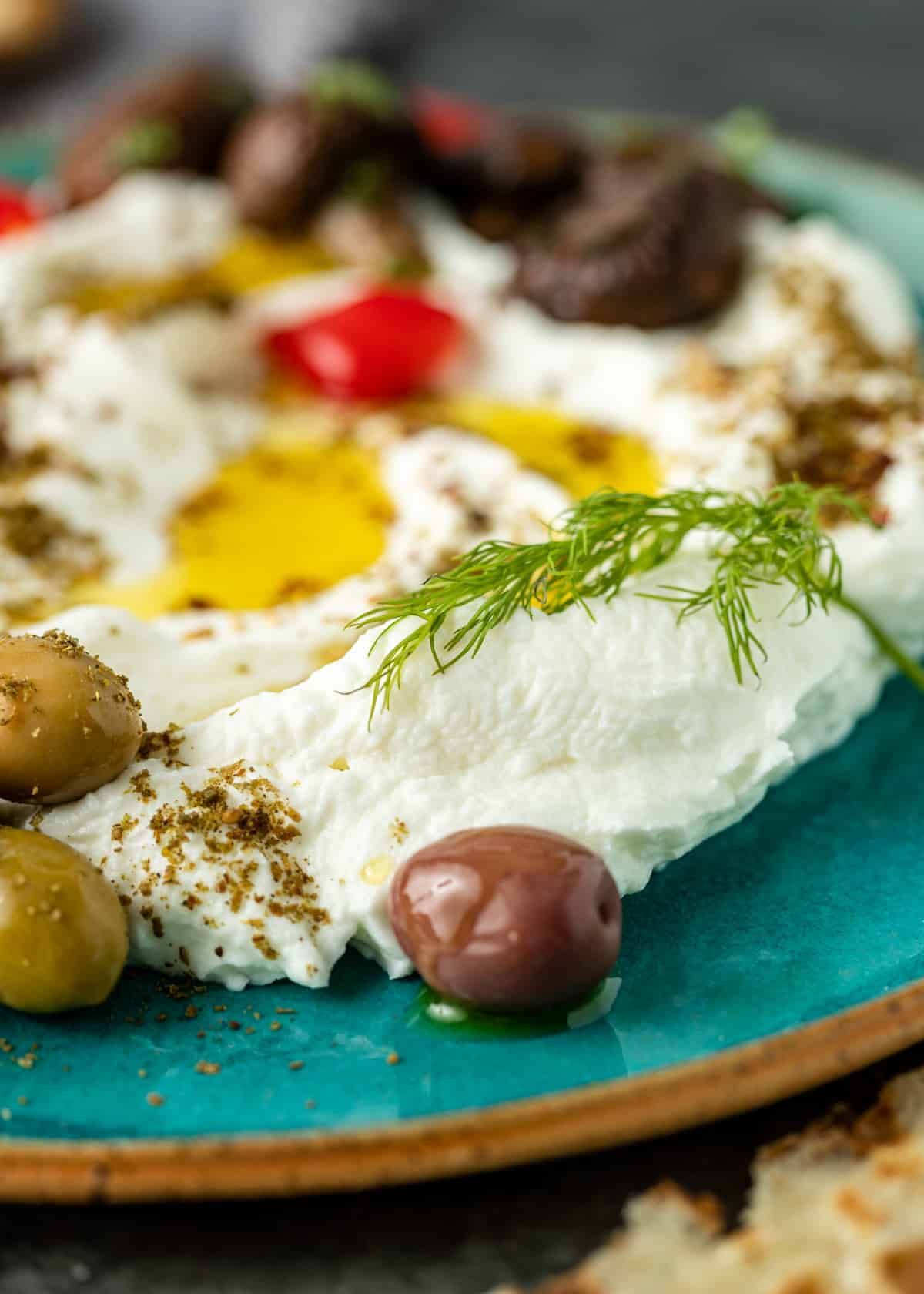 extreme close up of labneh topped with drizzle of olive oil, surrounded by green olives