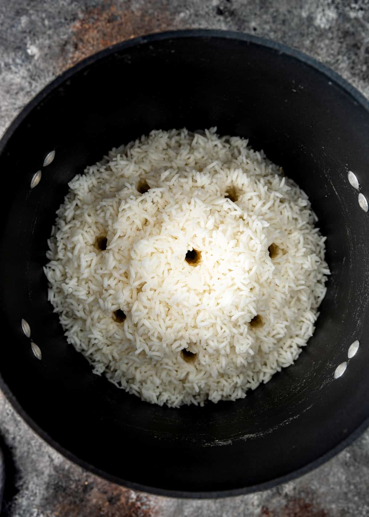 overhead image: several small holes poked into pile of cooked basmati rice in a skillet
