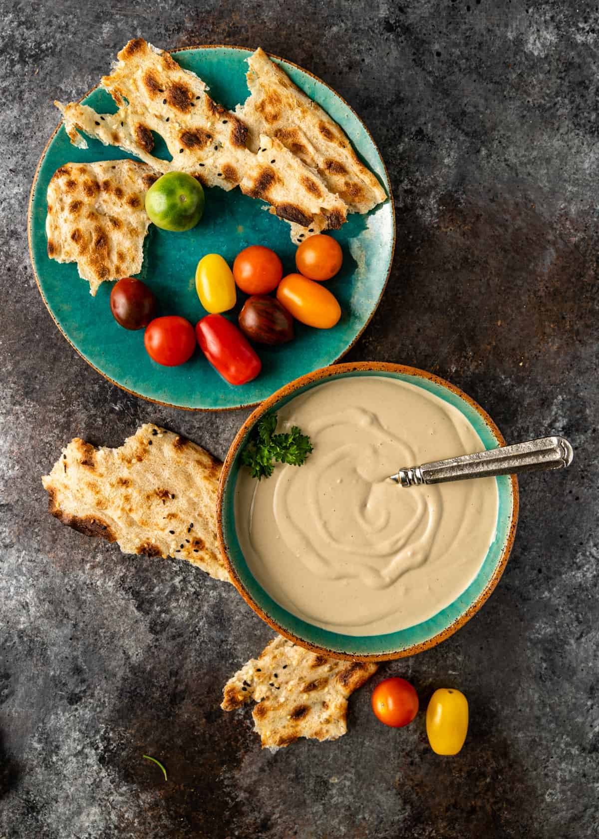 overhead of a bowl of tahini sauce with pita and tomatoes for dipping