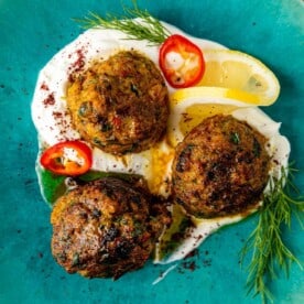 overhead: 3 fish meatballs sitting in homemade labneh on a blue plate