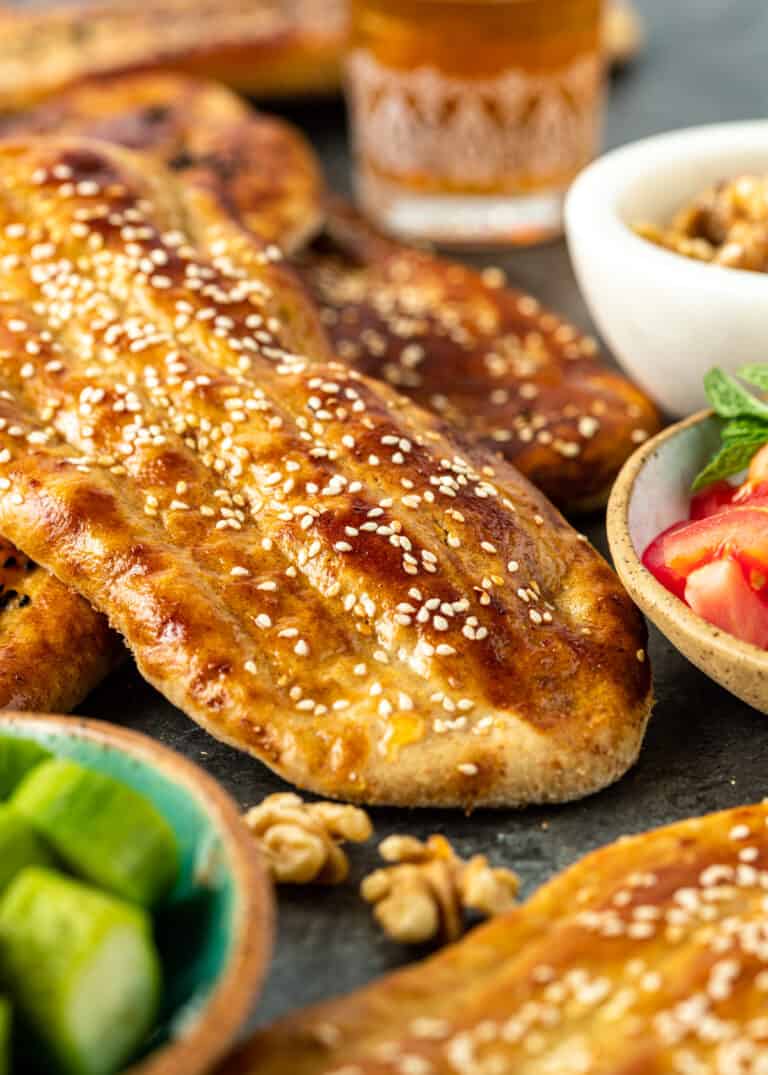 closeup: several loaves of barbari (griddle bread) topped with white sesame seeds