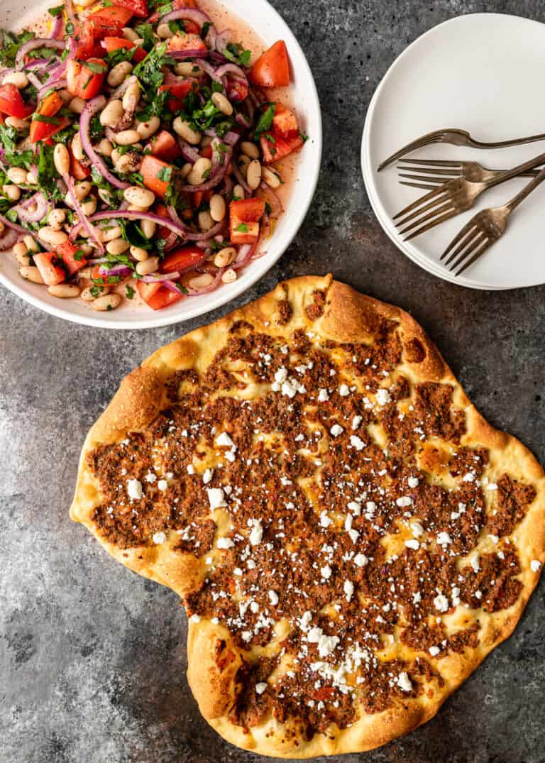 overhead image: Turkish pizza next to bowl of 4 bean salad, serving plates and forks