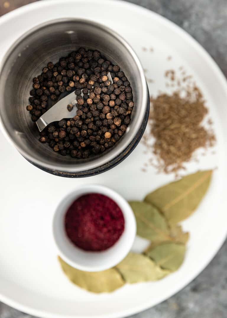 ingredients for a turkish spice blend with peppercorns, cumin seeds, turkish bay leaves, sweet paprika, and sumac