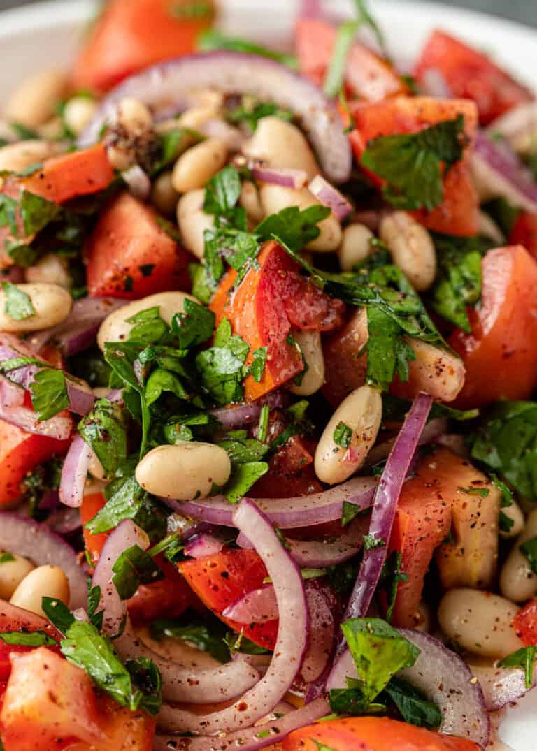 close up image of a salad with white beans, tomato, red onion, Italian parsley and spices
