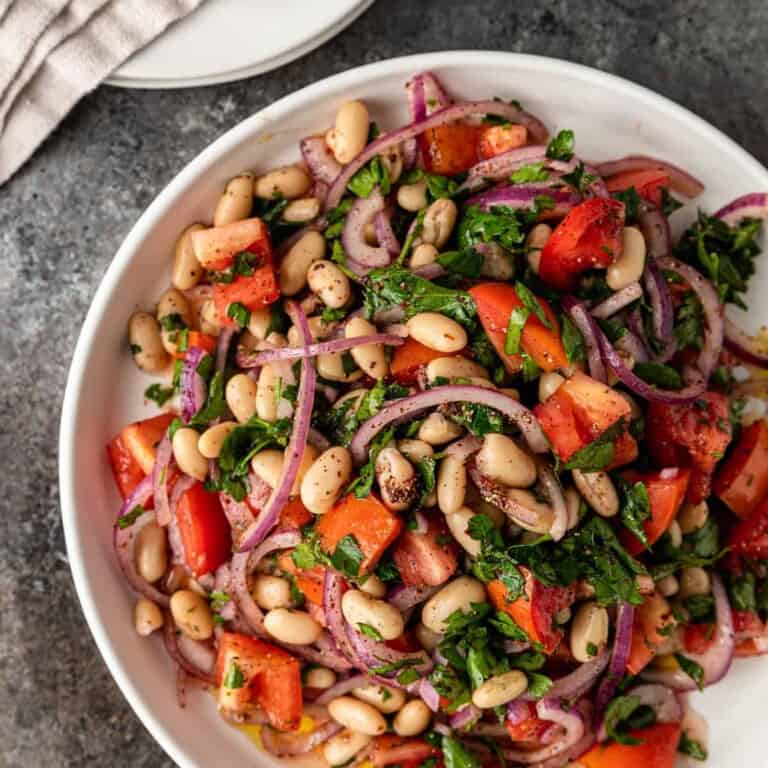 white plate loaded with a salad with white beans, tomato, red onion, Italian parsley and spices