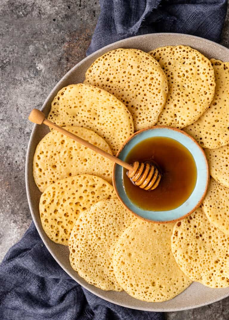 overhead image: semolina pancakes arranged on platter in circular pattern around a bowl of honey