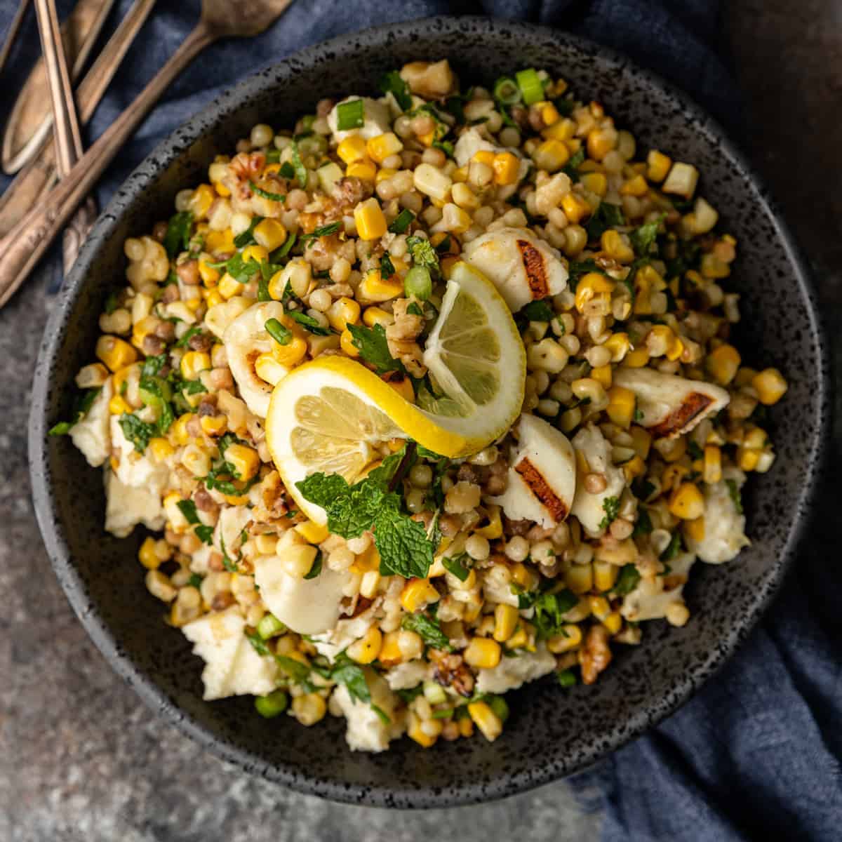 fregola salad with grilled halloumi and corn in large black serving bowl