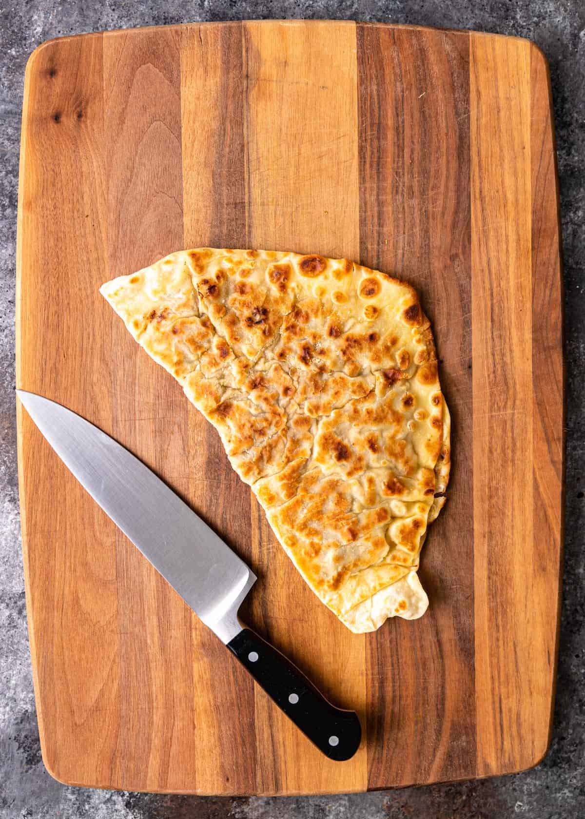 overhead: crispy homemade flatbread on cutting board with chef's knife