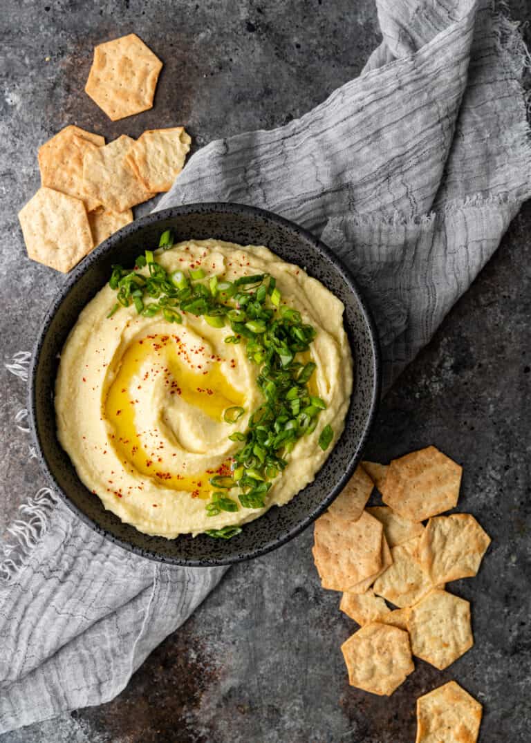 overhead image: creamy potato and garlic dip recipe served in black bowl surrounded by hexagon shaped crackers
