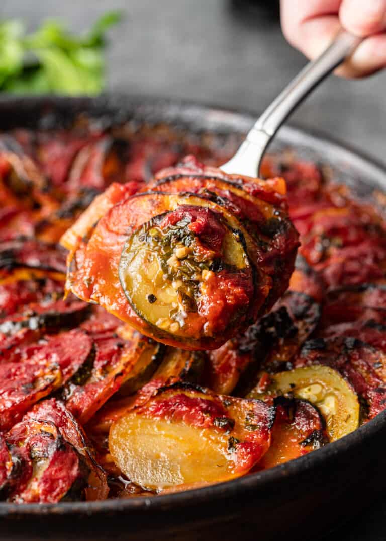 serving spoon of baked tomato, zucchini and eggplant casserole