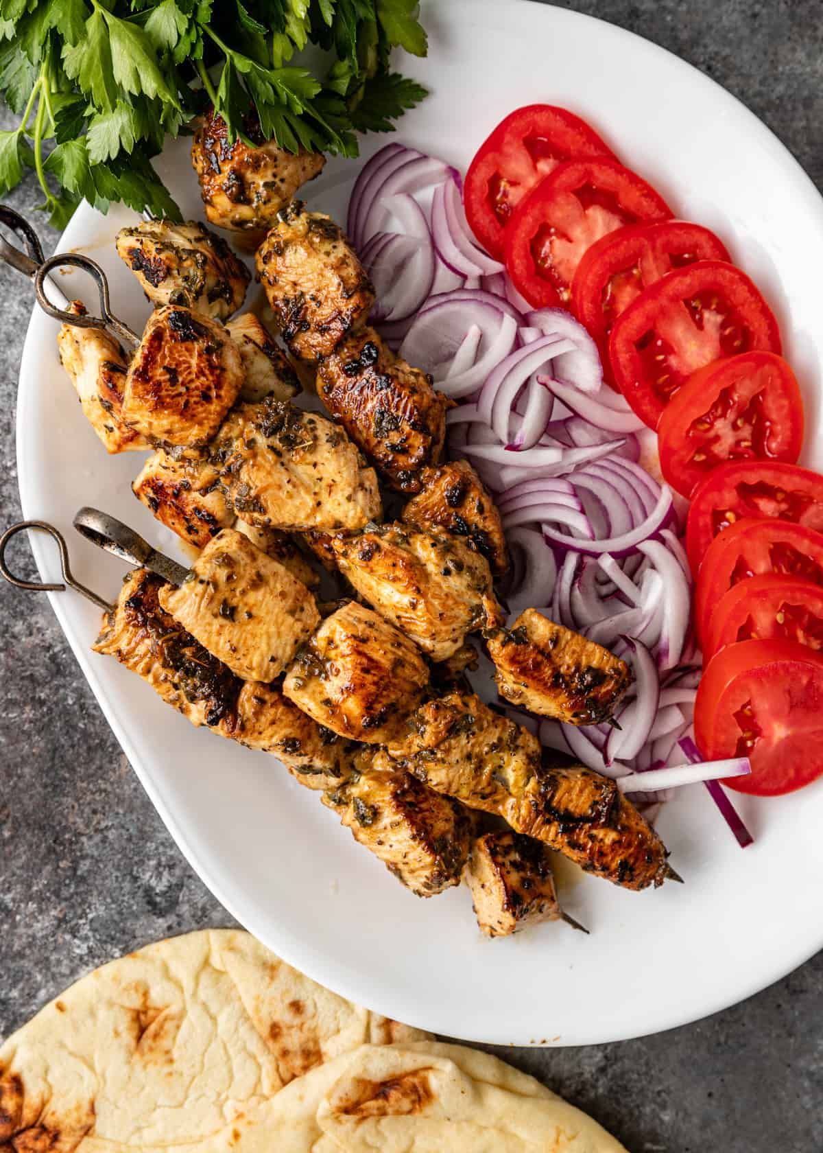 overhead: white platter with grilled chicken on skewers, red onion slices and tomato slices