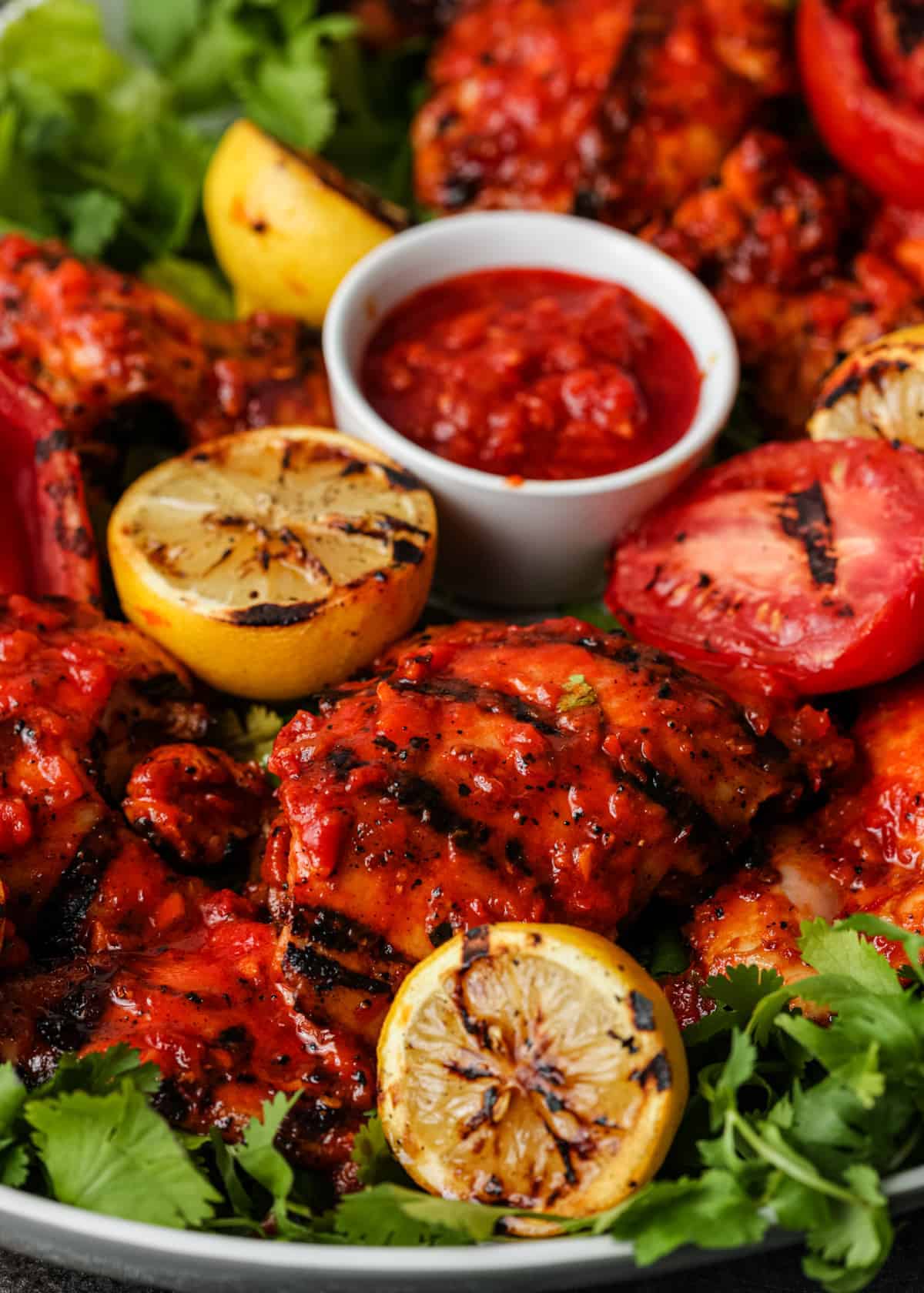 closeup image: spicy grilled chicken on platter with grilled lemon halves