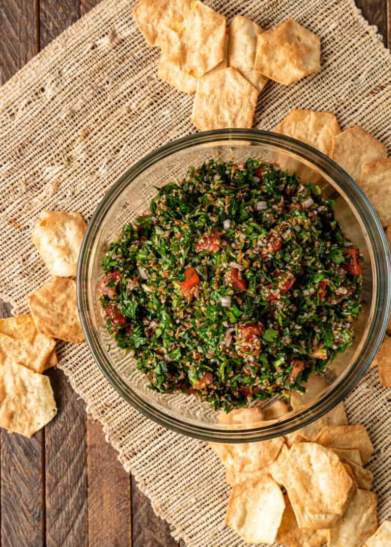 overhead: healthy bulgur and parsley tabouli salad in glass bowl surrounded by pita chips