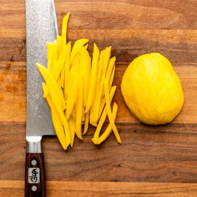 overhead: julienne strips of green mango and a large Chef's knife on cutting board