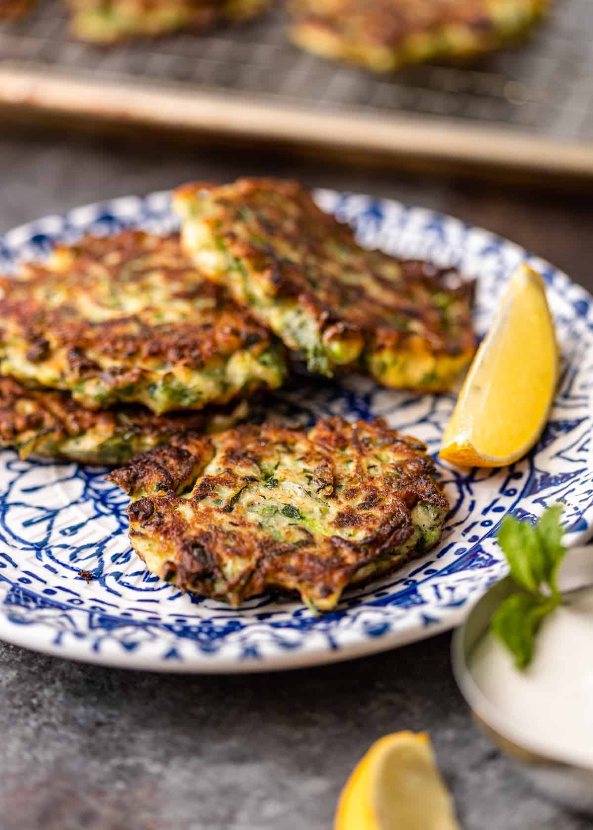 4 Greek zucchini pancakes on small blue and white plate with lemon wedge
