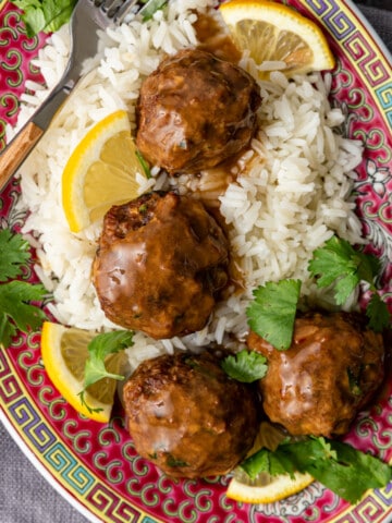 overhead image: plate of Asian lemon cilantro chicken meatballs served over white rice with lemon slices