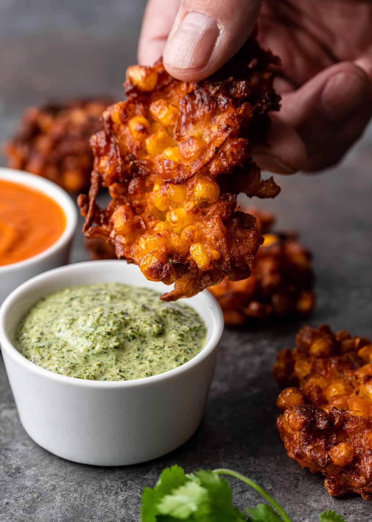 dipping Indian corn fritter into dish of creamy mint chutney