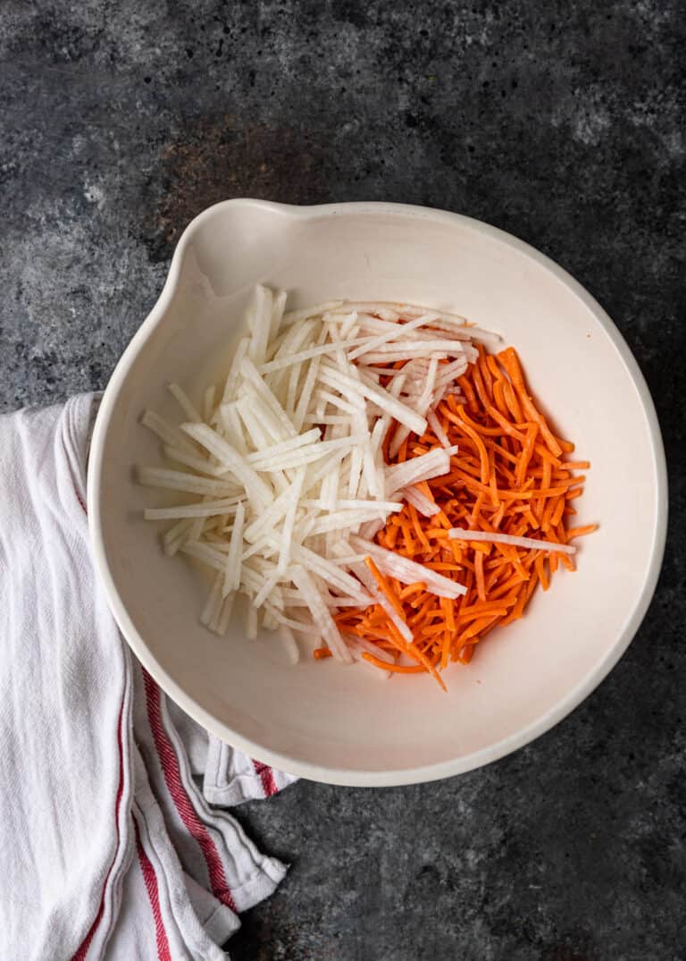 overhead: julienne cut carrots and onion in white mixing bowl