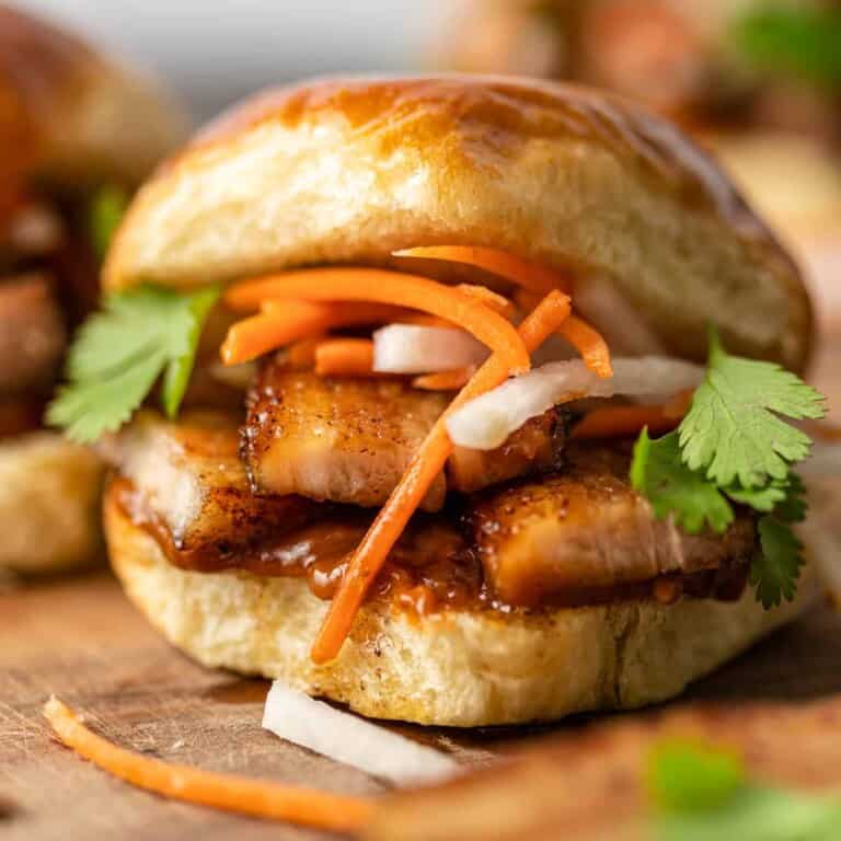 close up: fried pork belly on a soft bun with thin slices of carrots and onions
