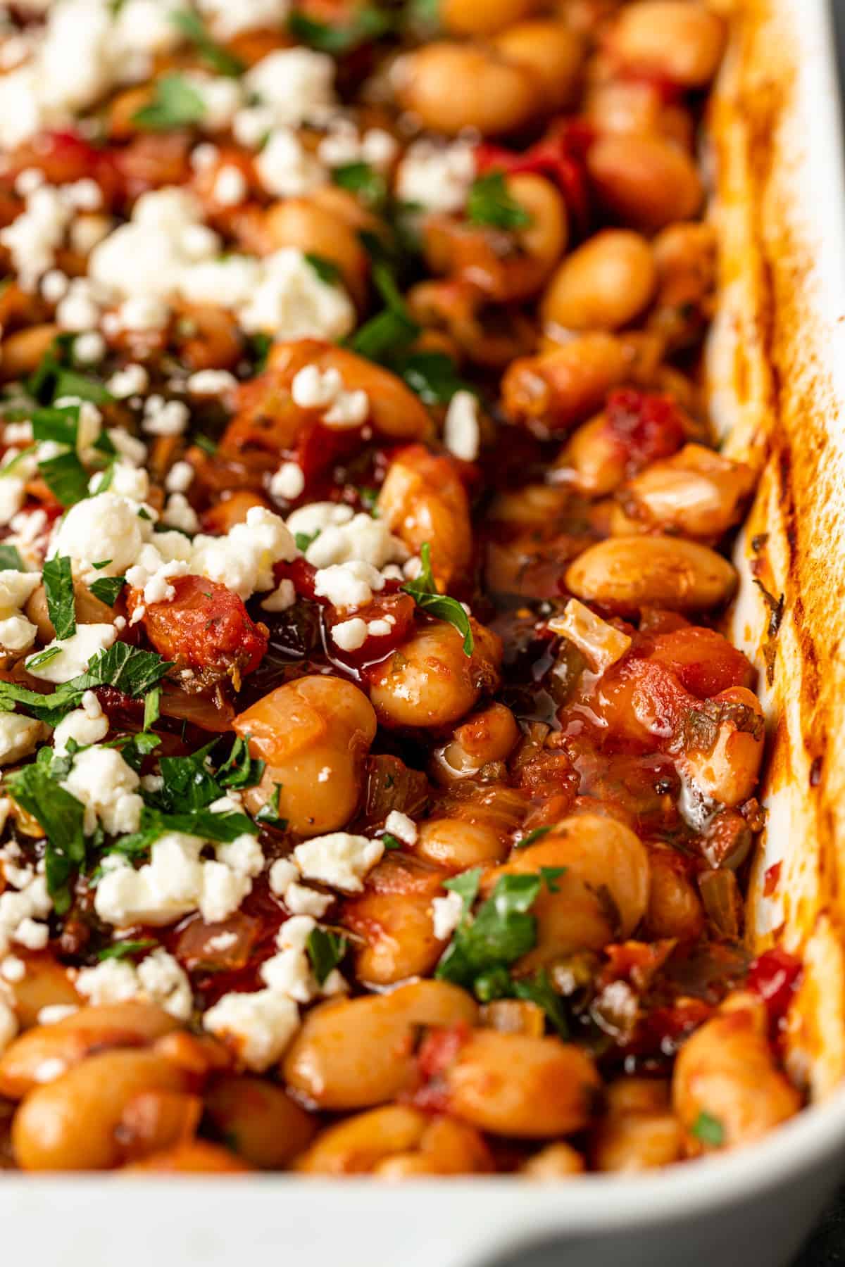 overhead: casserole dish of Greek baked beans in tomato sauce with parsley and feta cheese