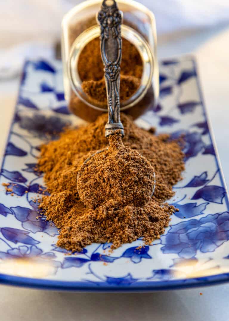 spoonful of ground spices balanced against spice jar on blue and white plate