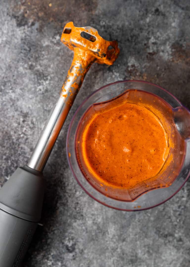 immersion blender laying next to container of smooth red sauce