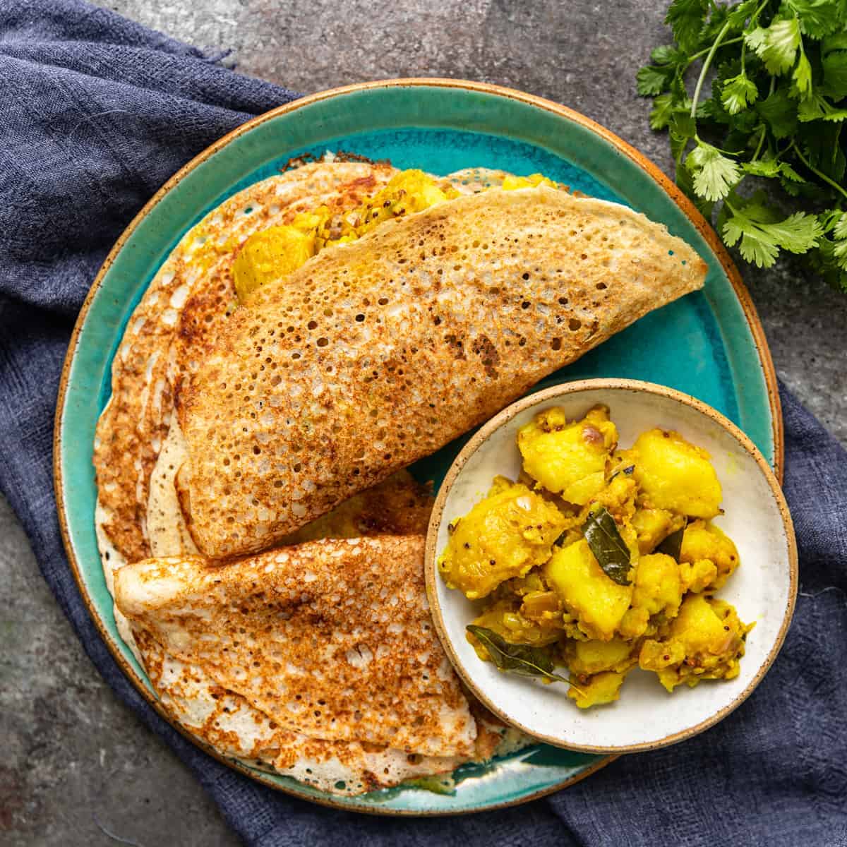 green plate with stack of Indian crepes and spicy potatoes