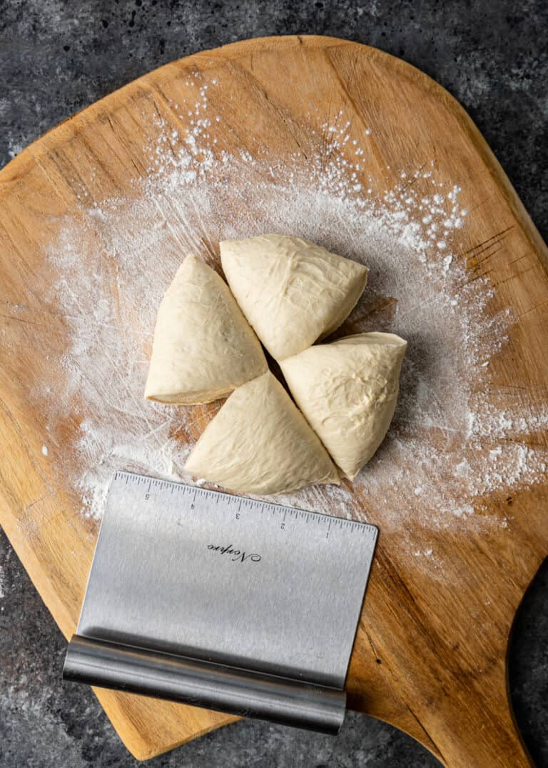 overhead: four portions of pizza dough on floured wooden cutting board