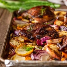 crispy roasted chicken thighs on baking sheet with slices of fennel, sweet potatoes and red apple