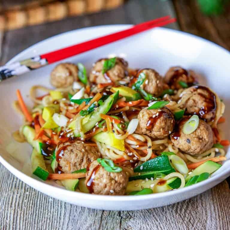 asian pork meatballs drizzled with sauce in white bowl with noodles and vegetables