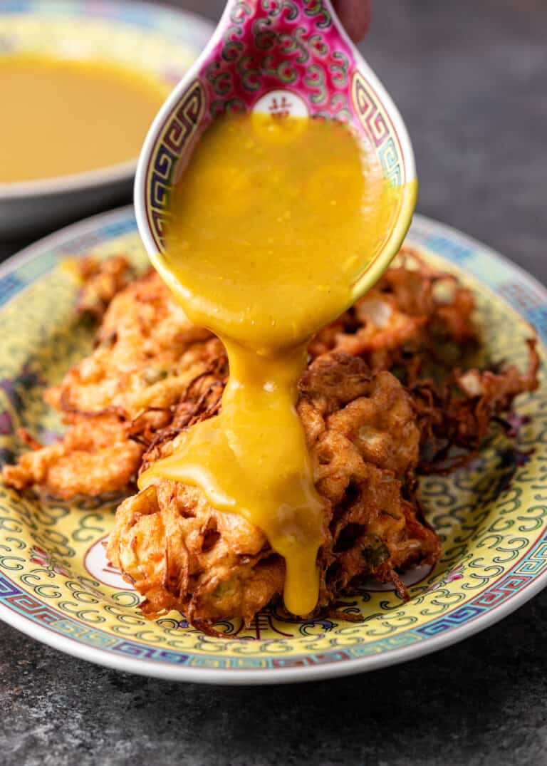 spooning yellow sauce over chicken egg foo young on platter