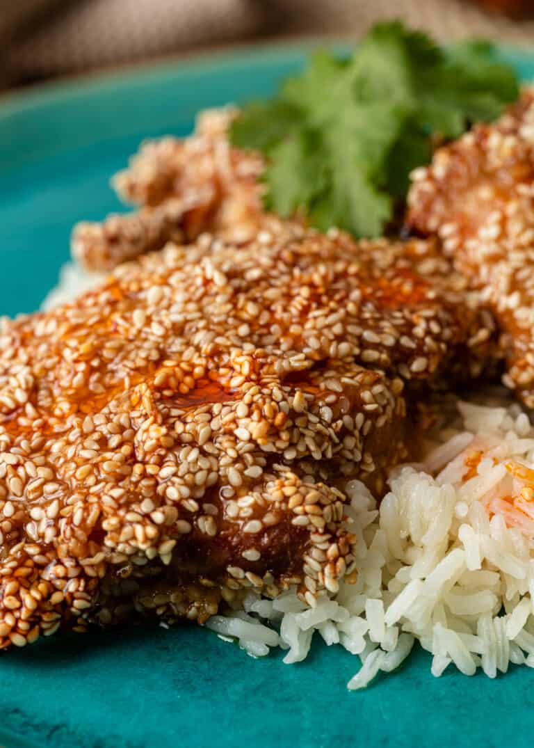 cooked chicken breasts coated with sesame seeds, plated on bed of white rice
