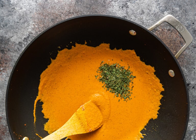 overhead: stirring orange colored masala in saute pan
