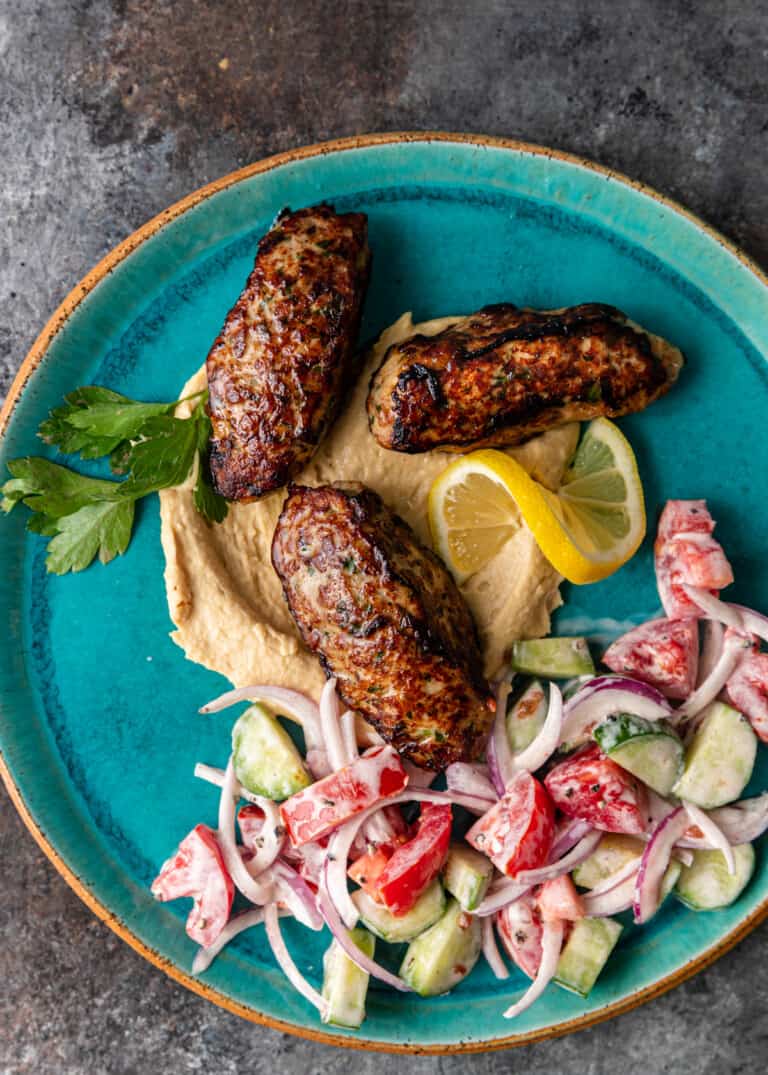 over head shot of 3 chicken kofta on a plate of hummus and salad