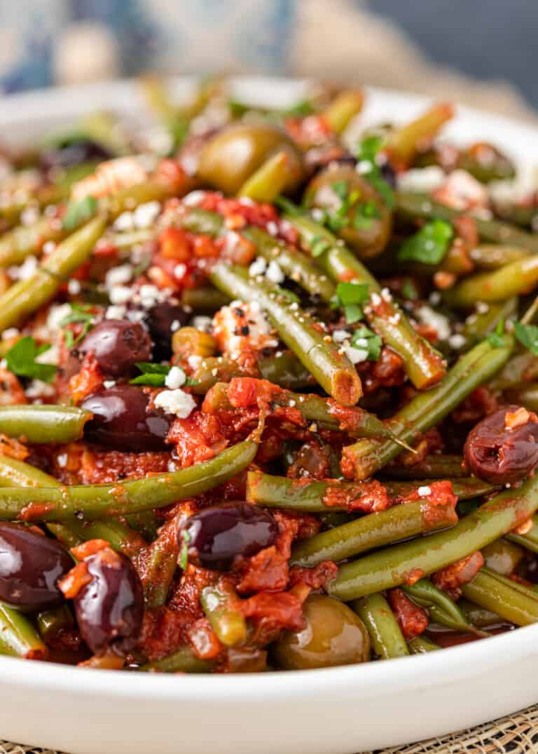 close up of Fasolakia, or Greek green beans in a flavorful tomato sauce topped with olives and feta cheese.