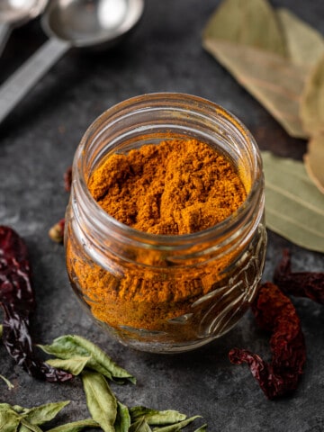 madras curry powder in glass jar on table with drie dchili and leaves
