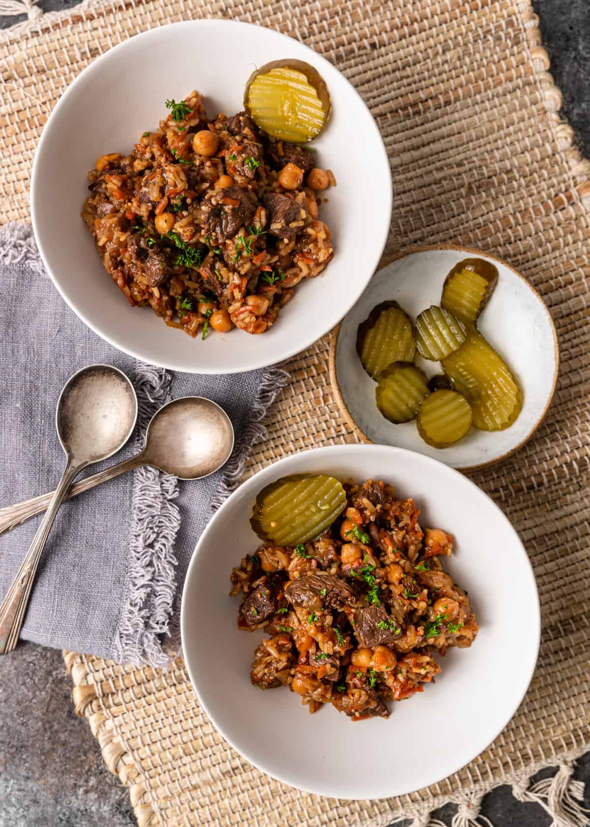overhead shot of beef plov in bowls and a plate with pickles