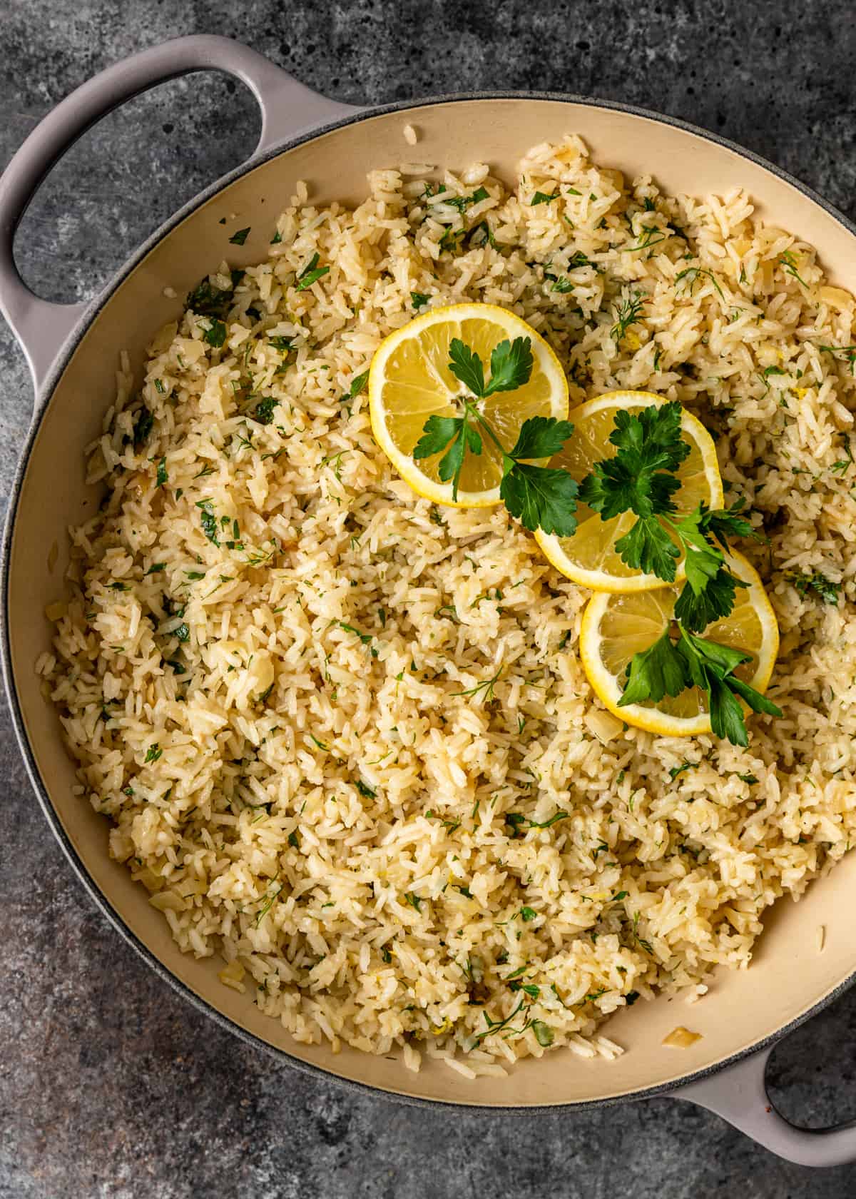 overhead view of a skillet with greek lemon rice, lemons, and herbs