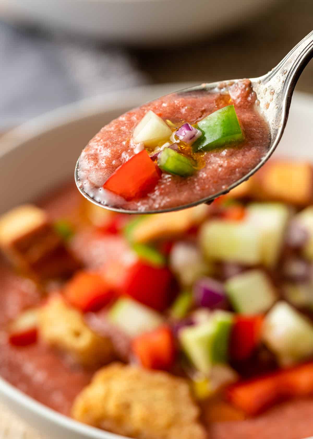 extreme closeup: a spoonful of gazpacho over a bowl of cold Spanish soup