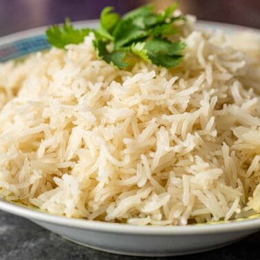 steamed white basmati rice in bowl with cilantro leaves