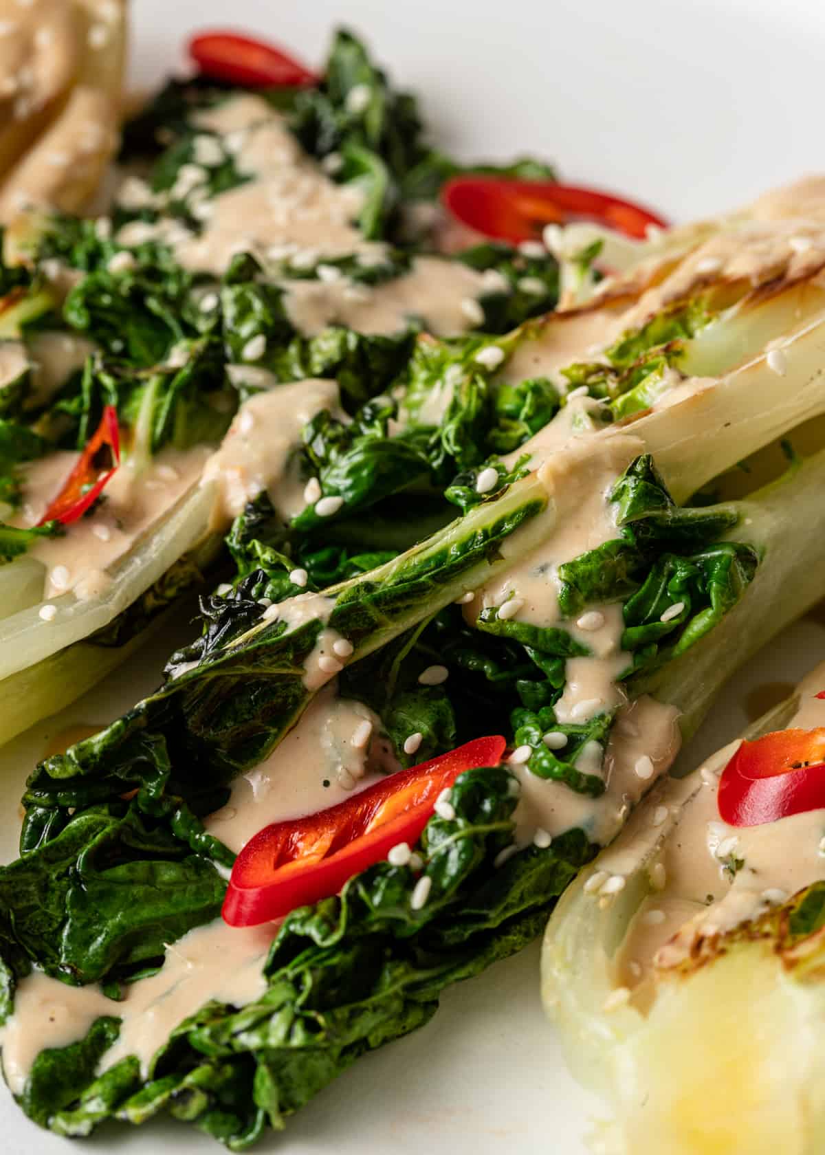 A close up of a salad with greens and small red peppers with miso tahini dressing on top.