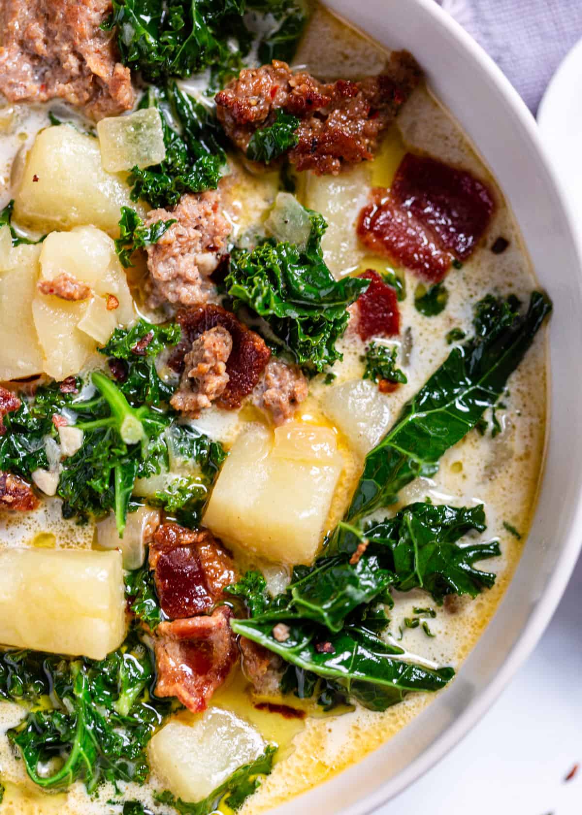 close up of zuppa toscana in a white bowl with potatoes, bacon, and greens visible