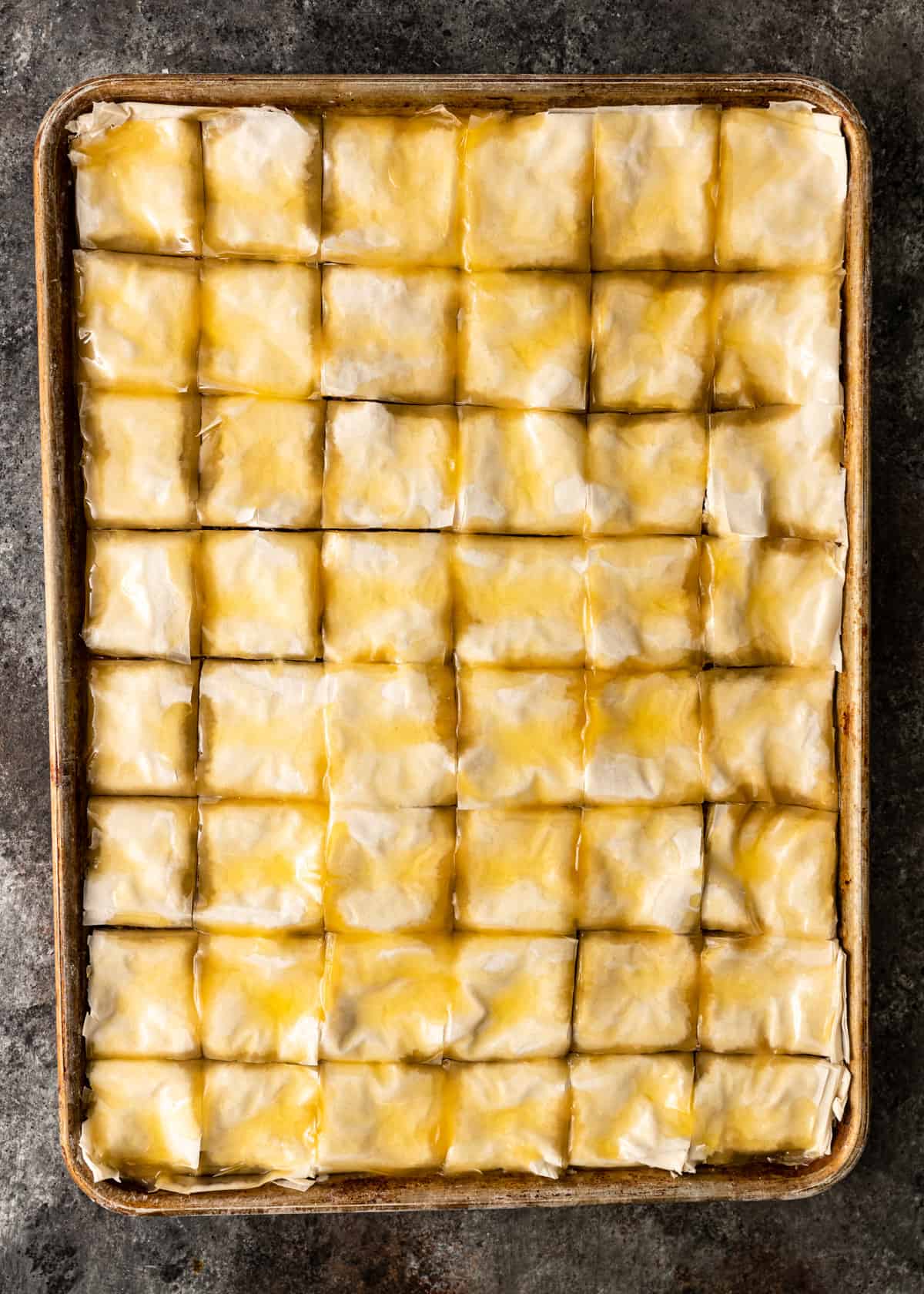 top down view of uncooked cut baklava on a baking sheet soaked in melted ghee or butter