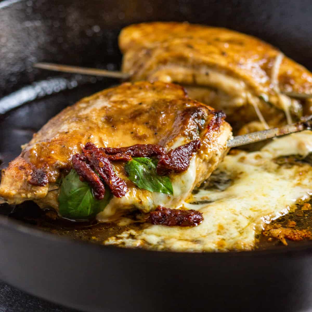 stuffed chicken caprese cooking in a skillet with melted mozzarella and sun-dried tomatoes
